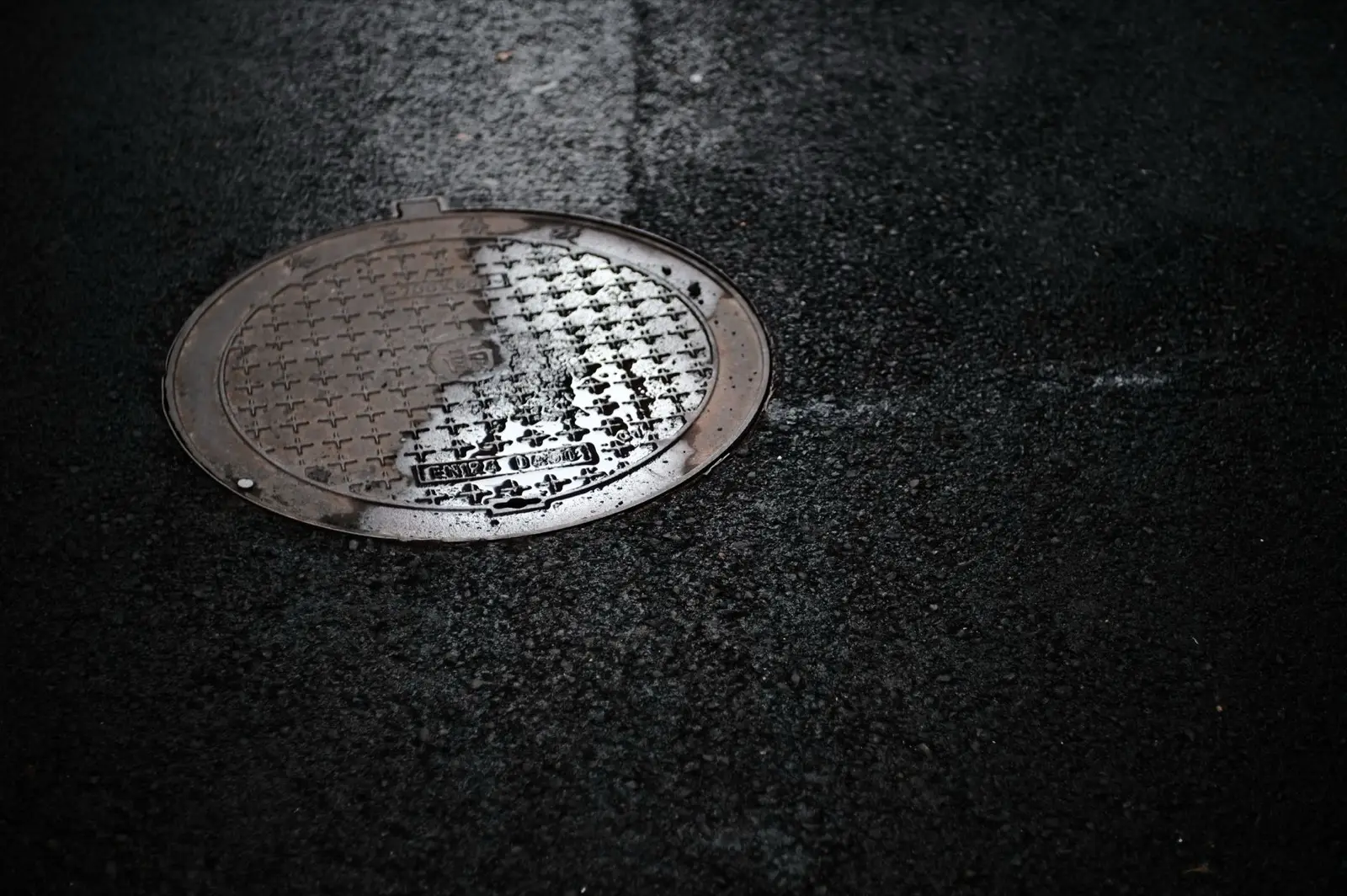 Plaque de regard en fonte sur une chaussée urbaine mouillée par la pluie, reflets de lumière